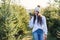 Joyful pretty young woman in warm hat photography beautiful christmas trees during walking among forestry plantings.