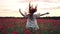 Joyful red-haired woman jumps up in flowered poppy field at sunset, slow motion