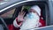 Joyful Santa Clause in Covid-19 face mask waving looking at camera sitting in car on driver's seat. Modern Caucasian