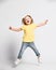 Joyful screaming loud kid baby girl blonde with handband in yellow t-shirt and blue jeans is jumping high, having fun
