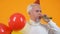 Joyful senior man party hat blowing noisemaker holding balloons, celebration