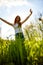 joyful slender woman posing in a field with her arms raised high