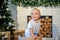 Joyful smiling baby boy in white t-shirt with bear standing in basket near fireplace and looking away in christmas time at home.