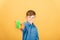 A joyful and smiling boy in a blue shirt and orange gloves shows a washing sponge in green on a yellow background