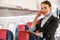 Joyful stewardess standing by overhead luggage bin in aircraft