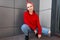 Joyful stylish young woman with hairstyle in a trendy red bandana in a fashionable red hoodie in vintage jeans