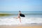 Joyful surfer girl happy cheerful running surfing at ocean beach water. Female bikini heading for waves with surfboard