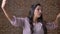 Joyful talking caucasian female is holding smartphone in one hand and having video call, standing relaxed, brick behind