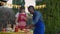 Joyful teenage daughter clapping and helping serious father preparing picnic burgers outdoors. Portrait of friendly