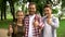 Joyful teenagers and their father showing thumbs up into camera at park, family