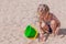 Joyful three-year-old girl plays with a bucket and shoulder blade in the sand on the beach