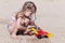 Joyful three-year-old girl plays with a machine in the sand on the beach