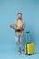Joyful traveler tourist man in yellow casual clothes with photo camera, suitcase isolated on blue background. Male