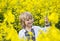 Joyful Ukrainian boy of 6 years old in a traditional embroidered shirt stands among a yellow flowering rapeseed field