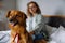 Joyful white woman smiling while lying on sofa at home with her dog