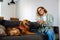 Joyful white woman using cellphone while sitting on sofa with her dog