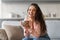 Joyful woman laughing while holding cup, in cozy home setting