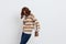 a joyful woman stands on a white background in a striped sweater and a bag on her shoulder , put her second hand on the