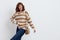 a joyful woman stands on a white background in a striped sweater and a bag on her shoulder , put her second hand on the