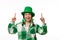 Joyful woman wearing clover leaf earrings and green hat for St. Patrick's pub party, points fingers up white