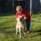 Joyful Yakut fat woman in glasses playing with his dog breed Akita inu on the green grass of the village