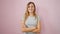 Joyful young blonde woman, cheerfully smiling, standing with crossed arms over an isolated pink background - a vibrant expression