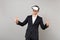 Joyful young business man in classic black suit, shirt looking in headset, showing thumbs up isolated on grey wall