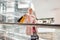 Joyful young fashion model woman in luxurious pink fur coat in leather glamorous fashionable skirt on escalator in modern store.