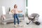 Joyful young maid with mop posing and smiling at camera in middle of tidy apartment, copy space