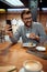 Joyful young man enjoying coffee at coffee shop, listening to music, smiling. Modern industrial interior design background