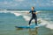 Joyful young woman beginner surfer with blue surf has fun on small sea waves. Active family lifestyle, people outdoor