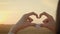 Joyful young woman make heart shape hand gesture at sunset in wheat field