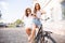 Joyful young women riding a bicycle together. Best friends having fun on a bike at the river promenade in the cit.