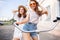 Joyful young women riding a bicycle together. Best friends having fun on a bike at the river promenade in the cit.