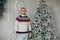 Joyous gentleman in warm sweater standing near Christmas tree