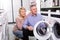 Joyous mature couple chooses washing machine for their house in shop of household appliances