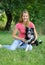 Joyous woman in pink shirt and blue jeans playing with her white and black dog in the park during sunny summer day