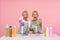 Joyous young lovely blonde cleaning ladies looking happily at camera with wide smiles while posing over pink background with spray