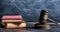 Judge gavel, old books and reading glasses on a wooden table, black board background. 3d illustration