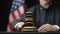 Judge`s hand with wooden gavel hammering against American flag in United States court