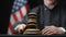 Judge`s hand with wooden gavel hammering against American flag in USA court room