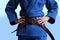 Judo girl with brown belt. A judoka teenager fighter poses in a blue kimono on a plain background. Japanese martial art.