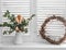 Jug of dried eucalyptus branches, vine wreath on a window with wooden blinds in a bright room. Comfort home decoration concept