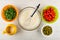 Jug of milk, bowls with spinach, sweet pepper, green peas, bowl with whipped eggs and whisk on table. Top view