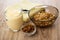 Jug with yogurt, bowl with muesli, spoon on napkin, bowl with raisin on table