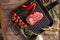 Juicy, aged raw ribeye steak in a grill pan with red chili peppers, rosemary, red tomatoes on a branch, a head of garlic, burlap,