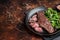 Juicy Grilled Machete skirt beef meat steak on plate with salad. Dark background. Top view. Copy space