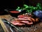 Juicy grilled piece of meat on a cutting board, basil, parsley, spices,vintage knife and fork on a da on a dark background