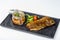 A juicy large piece of grilled fish sits on a square black plate.