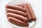 Juicy meat sausages in a group on a white plate. Delicious semi-finished sausages. Delicious breakfast